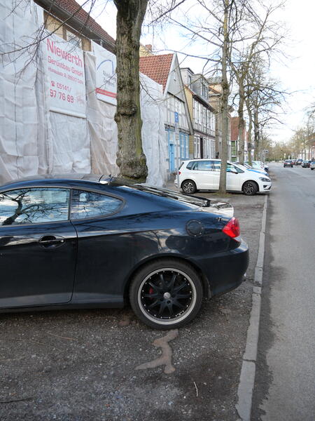 Ein Auto parkt direkt auf einer Baumwurzel in der Breiten Straße in Celle.